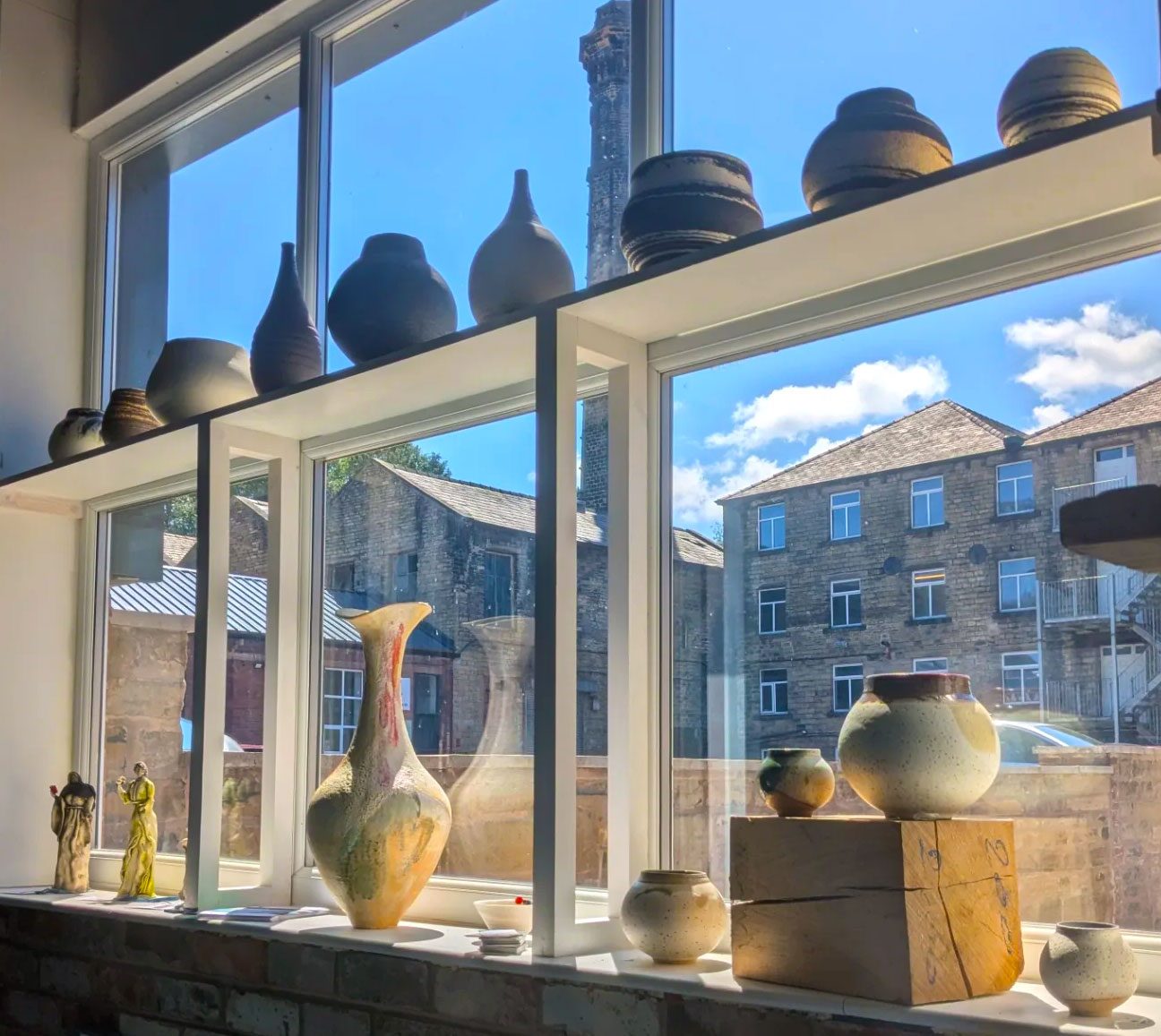 A selection of ceramic pots displayed on a window ledge with the sun glinting through the window and lighting them up.